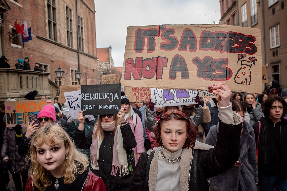 Person zeigt auf Demozug Schild mit der Aufschrift "It's a dress not a yes"