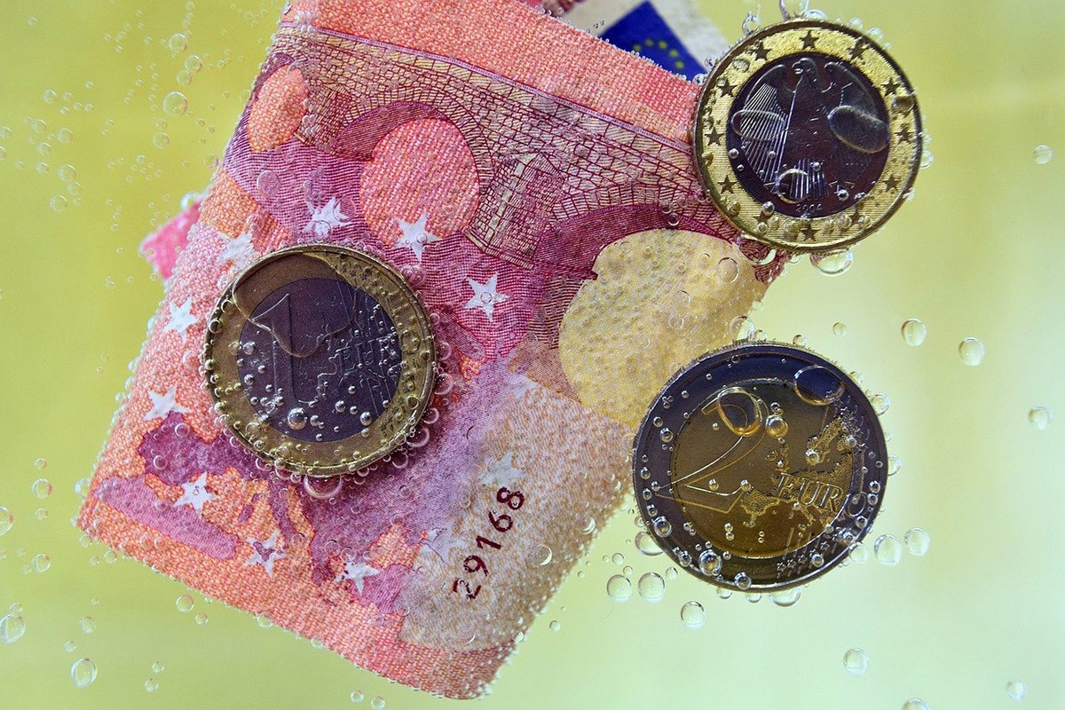 Geldschein und Münzen im Wasser mit Bläschen