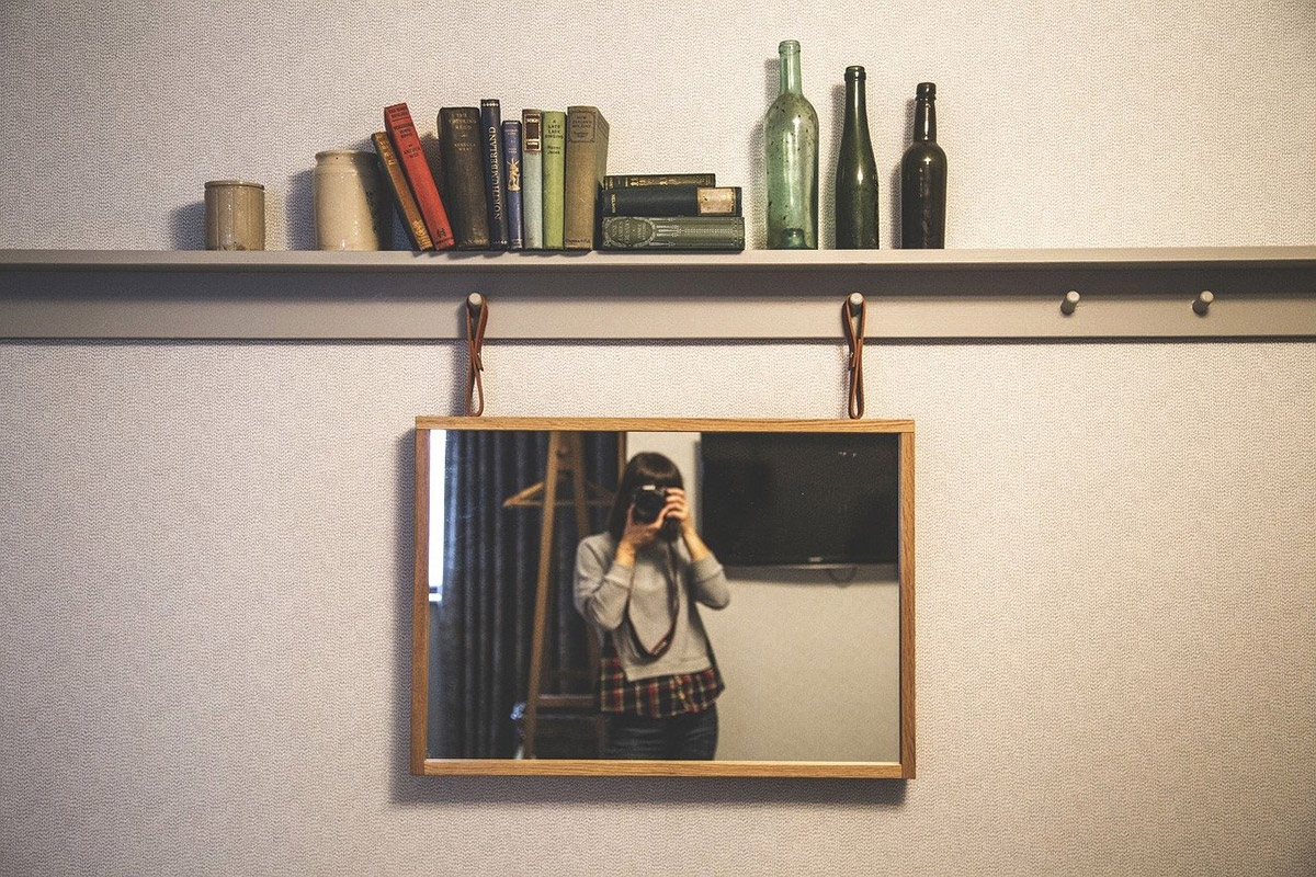 Frau mit Kamera in der Hand fotografiert sich selbst im Spiegel