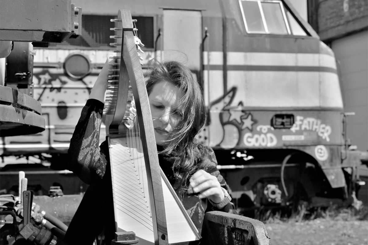 Ann Eysermans spielt Harfe, hinter ihr eine alte Diesellok