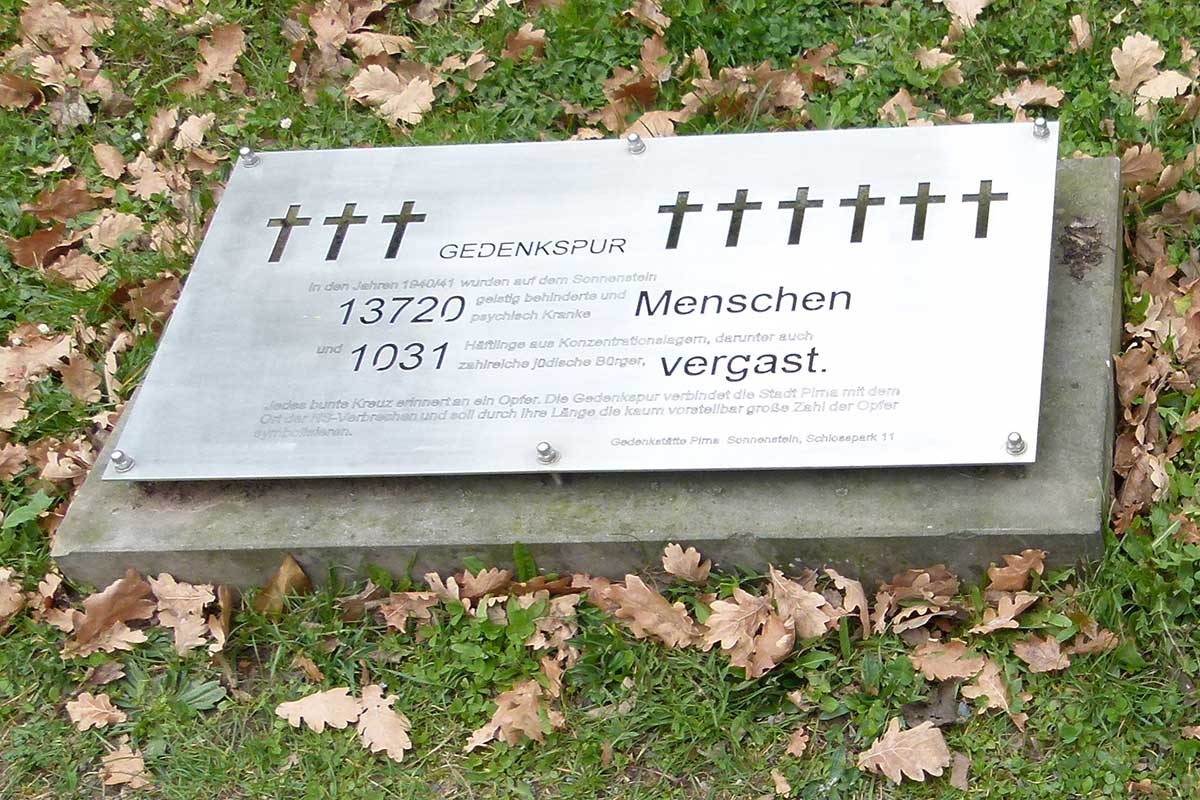 Informationstafel zur sogenannten Gedenkspur mit bunten Kreuzen für die in Pirna-Sonnenstein ermordeten Menschen