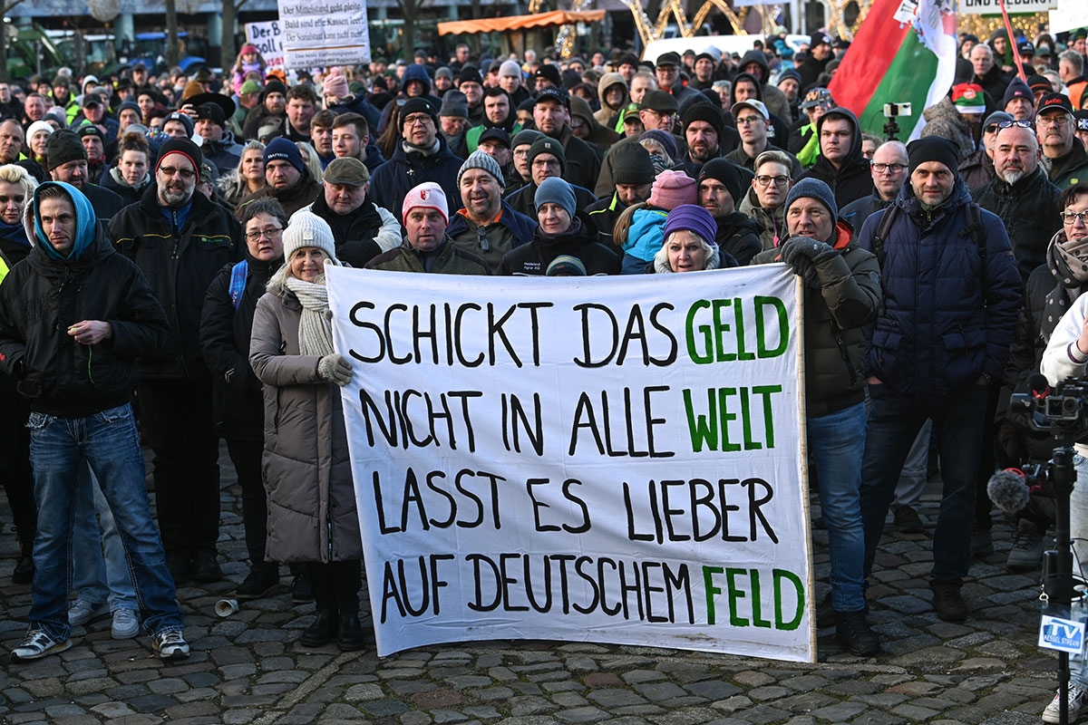 Teilnehmer der Kundgebung auf dem Domplatz halten ein Transparent mit der Aufschrift "Schickt das Geld nicht in alle Welt, lasst es lieber auf deutschem Feld". 
