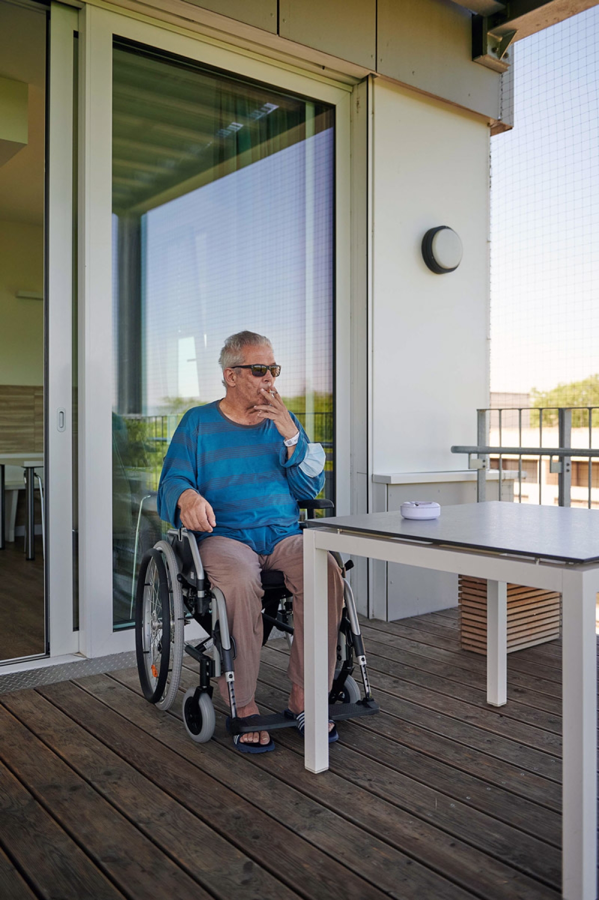 Ein Mann im Rollstuhl raucht auf einem Balkon