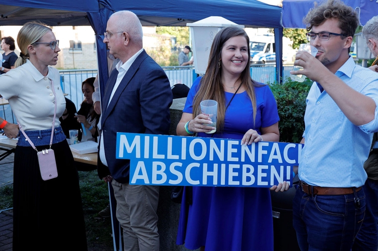 Menschen auf AfD-Wahlparty mit Schild "Millionenfach abschieben"