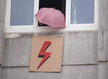 Geöffnetes Fenster aus dem ein Schild mit Blitz und ein Regenschirm ragen