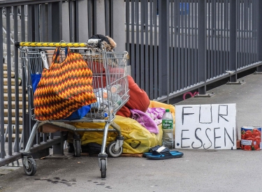 Ein Obdachloser sitzt mit seiner Habe an den Landungsbruecken in Hamburg auf dem Boden.Vor sich hat eine Dose und Schild gestellt mit der Aufschrift: Fuer Essen