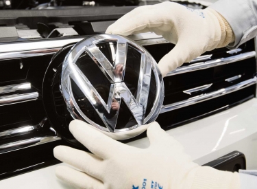 Ein Mitarbeiter montiert das VW-Logo an einen Neuwagen, Wolfsburg, 1. März