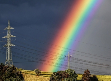 Regenbogen über einer Wiese mit Strommast