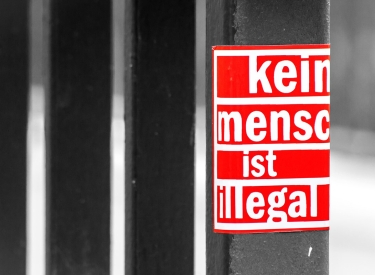 Roter Aufkleber auf Gitter "Kein Mensch ist illegal"