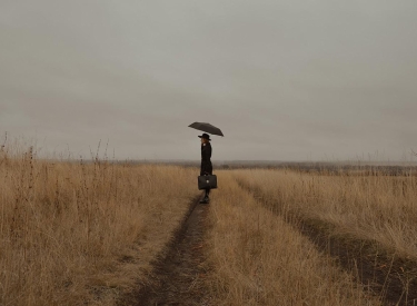 Frau mit Regenschirm steht auf einem Feld