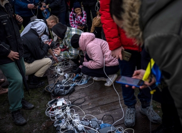 An Kabelknäueln und Mehrfachsteckern auf dem Boden laden Menschen ihre Telefone