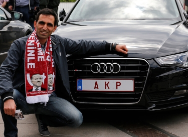 Ein Mann posiert vor einem Auto mit Nummernschild "AKP"