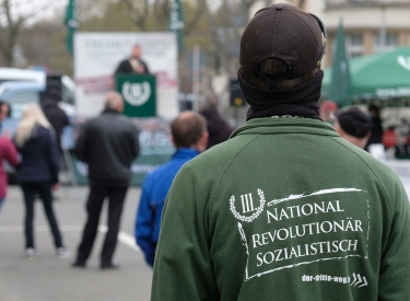 Ein Teilnehmer einer Kundgebung der rechtsextremen Partei „Der III. Weg“ trägt eine Jacke mit der Aufschrift "National revolutionär sozialistisch". 